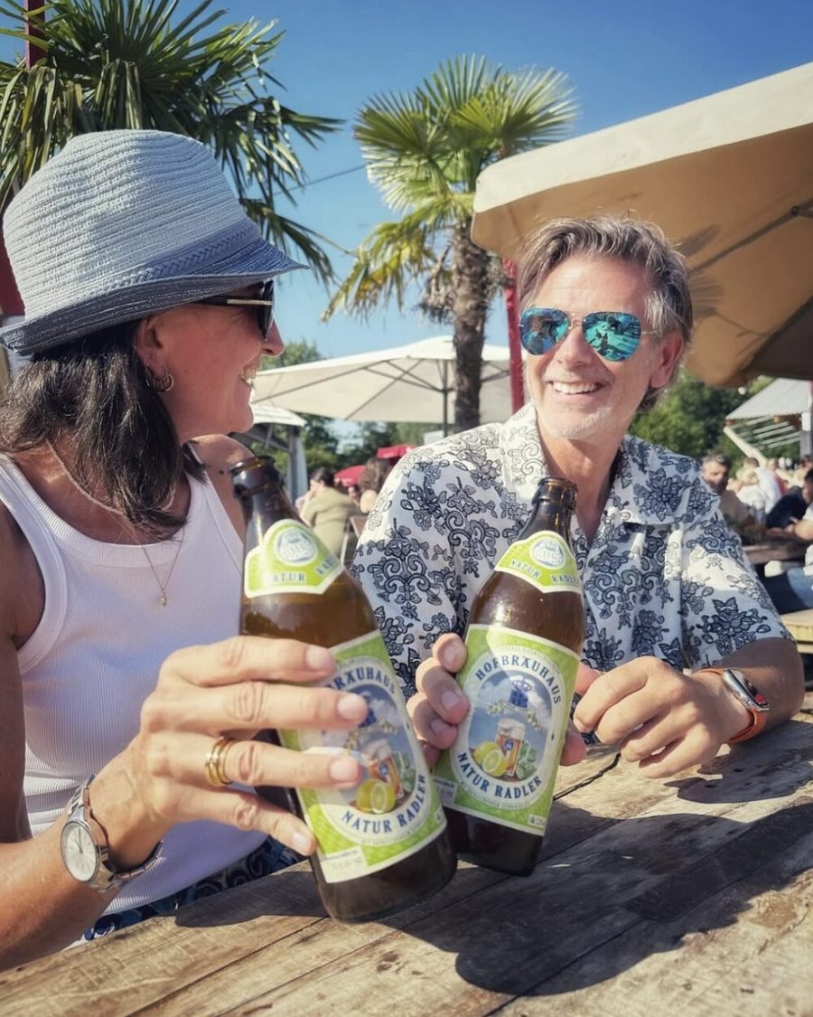 Zwei Gäste stoßen mit Hofbräu-Flaschen an, im Hintergrund Palmen